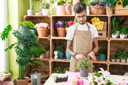 Photo for Young hispanic man florist cutting plant at flower shop - Royalty Free Image
