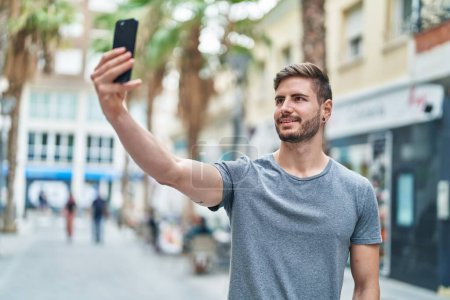 Téléchargez les photos : Jeune homme caucasien souriant confiant faire selfie par le smartphone à la rue - en image libre de droit