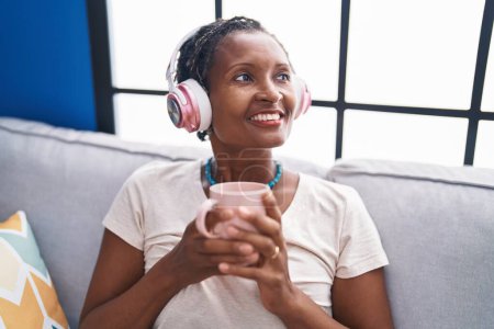 Foto de Middle age african american woman listening to music drinking coffee at home - Imagen libre de derechos