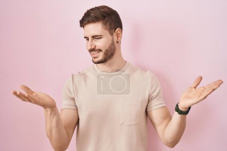 Téléchargez les photos : Homme hispanique avec barbe debout sur fond rose souriant montrant les paumes ouvertes des deux mains, présentant et comparant la publicité et l'équilibre - en image libre de droit
