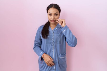 Téléchargez les photos : Jeune femme arabe en pyjama bleu bouche et lèvres fermées comme zip avec les doigts. secret et silencieux, tabou parlant - en image libre de droit