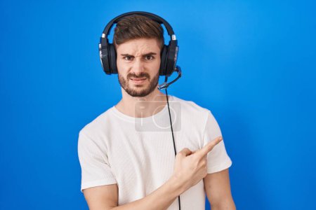 Photo for Hispanic man with beard listening to music wearing headphones pointing aside worried and nervous with forefinger, concerned and surprised expression - Royalty Free Image