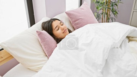 Téléchargez les photos : Une jeune femme hispanique dort paisiblement dans une chambre bien éclairée avec des oreillers blancs et roses. - en image libre de droit