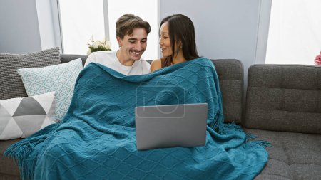 Interracial pareja disfrutando de tiempo junto con el ordenador portátil en acogedora sala de estar.
