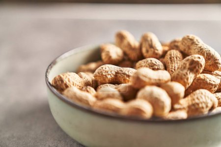 Foto de Primer plano de cacahuetes sin cáscara en un tazón en una mesa con textura, lo que sugiere un bocadillo saludable. - Imagen libre de derechos