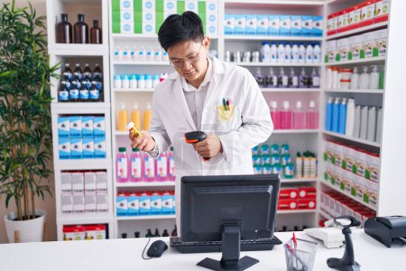 Foto de Joven hombre chino farmacéutico escaneo píldoras botella en la farmacia - Imagen libre de derechos