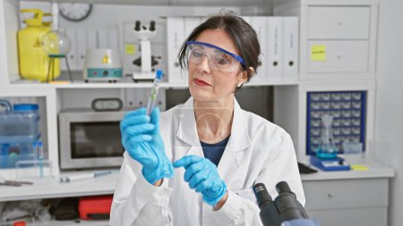 Téléchargez les photos : Femme scientifique hispanique senior examinant une éprouvette en laboratoire - en image libre de droit