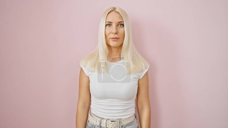 Téléchargez les photos : Jeune femme blonde fraîche et concentrée, exprimant une ambiance sérieuse, debout, détendu mais posé sur un fond isolé de mur rose. un portrait d'une beauté décontractée, captivant l'essence du style de vie. - en image libre de droit