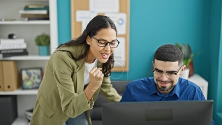 Foto de Celebrando el éxito, dos trabajadores enérgicos, un hombre y una mujer, se regocijan por el triunfo de su trabajo en la computadora en la oficina. - Imagen libre de derechos