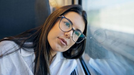 Foto de Joven mujer hispana hermosa pensando mirando a través de la ventana dentro de vagón de tren - Imagen libre de derechos