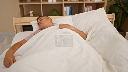 Foto de Hombre latino joven agotado encuentra consuelo sereno en casa, relajándose mientras se duerme en la acogedora cama de su dormitorio interior, descansando en medio del fondo de la tranquilidad de la mañana. - Imagen libre de derechos
