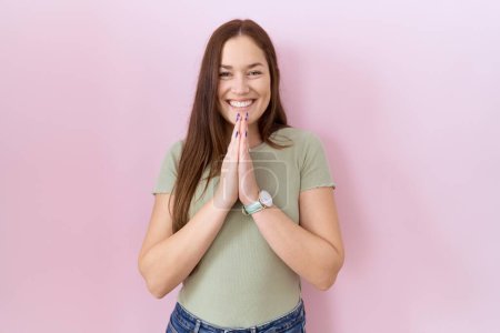 Photo for Beautiful brunette woman standing over pink background praying with hands together asking for forgiveness smiling confident. - Royalty Free Image