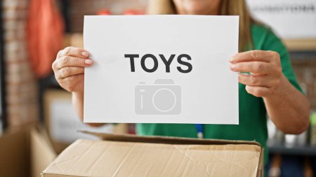 Photo for Middle age hispanic woman volunteer holding toys paper on cardboard box at charity center - Royalty Free Image