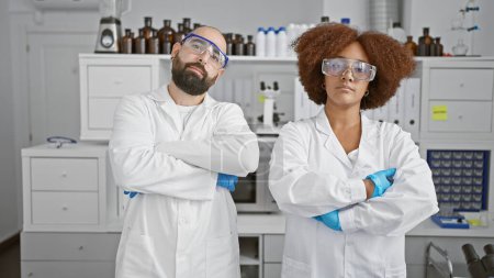 Téléchargez les photos : Deux scientifiques au visage sérieux, bras croisés, se tenant ensemble dans un laboratoire de haute technologie au milieu d'une recherche pionnière - en image libre de droit