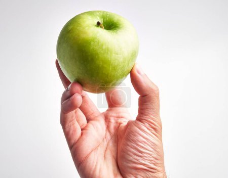 Foto de La mano de un hombre sosteniendo una manzana verde fresca sobre un fondo blanco, sugiriendo salud y nutrición. - Imagen libre de derechos