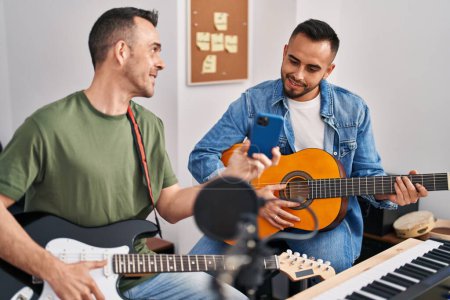 Téléchargez les photos : Deux musiciens hommes jouant de la guitare classique et électrique regardant l'écran du smartphone au studio de musique - en image libre de droit