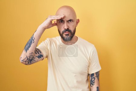 Téléchargez les photos : Homme hispanique avec des tatouages debout sur fond jaune inquiet et stressé par un problème avec la main sur le front, nerveux et anxieux pour la crise - en image libre de droit
