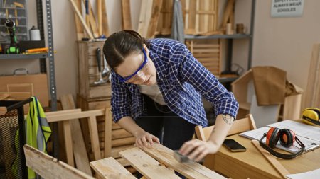 Photo for A focused woman in safety glasses working with wood in a carpentry workshop. - Royalty Free Image