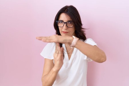 Photo for Middle age hispanic woman wearing casual white t shirt and glasses doing time out gesture with hands, frustrated and serious face - Royalty Free Image