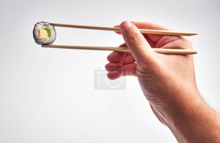 Photo for A man's hand skillfully holds sushi with chopsticks against a white background, capturing a culinary moment. - Royalty Free Image