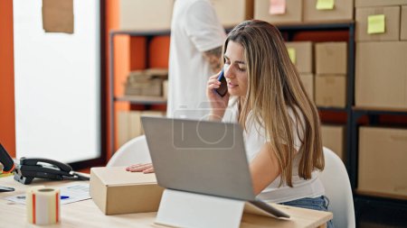 Téléchargez les photos : Deux travailleurs homme et femme utilisant un ordinateur portable parlant sur smartphone au bureau - en image libre de droit