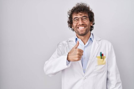 Téléchargez les photos : Jeune homme hispanique portant l'uniforme de médecin faisant des pouces heureux geste avec la main. approuvant l'expression regardant la caméra montrant le succès. - en image libre de droit