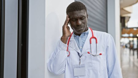 Téléchargez les photos : Médecin africain inquiet en milieu urbain extérieur tient la tête dans le stress - en image libre de droit