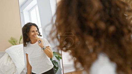 Photo for A mature hispanic woman with curly hair enjoys singing with a brush in her home bedroom. - Royalty Free Image
