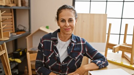 Photo for Mature hispanic woman with curly hair confidently poses indoors at a carpentry workshop. - Royalty Free Image