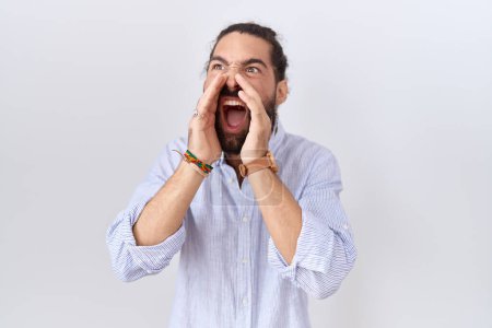 Téléchargez les photos : Homme hispanique avec barbe portant chemise décontractée criant en colère à haute voix avec les mains sur la bouche - en image libre de droit