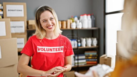 Téléchargez les photos : Jeune femme blonde bénévole souriant confiant parlant avec une personne au centre de charité - en image libre de droit