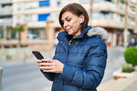 Téléchargez les photos : Femme d'âge moyen écoutant de la musique debout dans la rue - en image libre de droit
