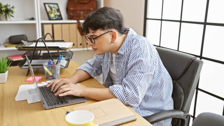 Téléchargez les photos : Jeune homme professionnel tapant sur ordinateur portable à son bureau organisé avec fond de fenêtre - en image libre de droit