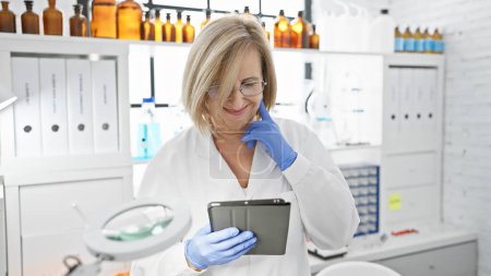 Photo for Smiling woman scientist with tablet in laboratory setting, surrounded by bottles and equipment. - Royalty Free Image