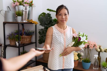 Photo for Young asian woman customer holding bouquet of flowers paying with dollars at flower shop - Royalty Free Image
