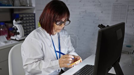 Foto de Mujer hispana de mediana edad con bata de laboratorio toma notas en una clínica, personificando la atención médica profesional. - Imagen libre de derechos