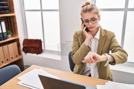 Téléchargez les photos : Young blonde woman business worker talking on smartphone looking watch at office - en image libre de droit