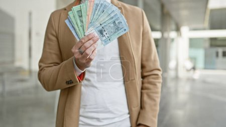 A stylish young man displays malaysian ringgit on a busy urban street, creating a dynamic portrait of commerce and fashion.