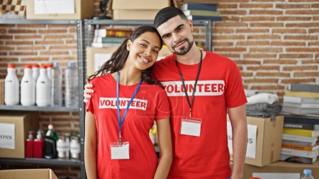 Photo for Smiling man and woman volunteers enjoy hugging each other, standing in charity center, unity in volunteer work - Royalty Free Image