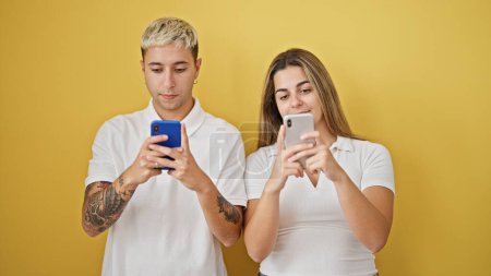 Photo for Beautiful couple using smartphones over isolated yellow background - Royalty Free Image