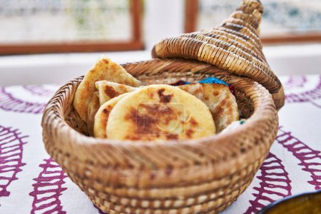 Téléchargez les photos : Panier à pain traditionnel en osier marocain rempli de khobz frais sur une nappe brodée. - en image libre de droit