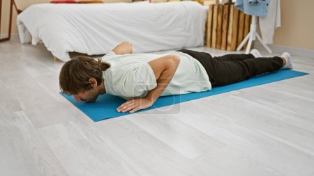 Photo for A young bearded man practices relaxation on a yoga mat in a tidy bedroom, epitomizing mindfulness and well-being. - Royalty Free Image