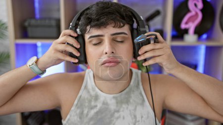 Téléchargez les photos : Jeune homme jouissant de musique avec écouteurs dans une salle de jeux moderne. - en image libre de droit