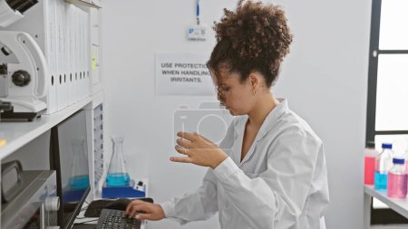 Foto de Mujer hispana con cabello rizado trabajando en un laboratorio, examinando una muestra química en el interior. - Imagen libre de derechos