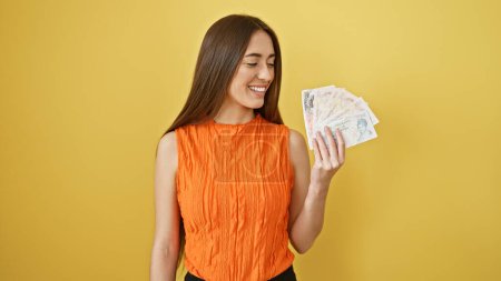 Téléchargez les photos : Femme souriante en haut orange tenant livres britanniques sur un fond jaune, dépeignant la finance et le bonheur. - en image libre de droit