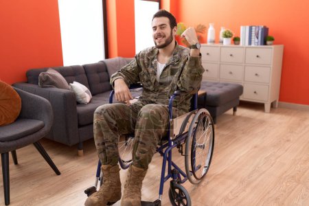 Téléchargez les photos : Jeune soldat hispanique homme blessé assis sur un fauteuil roulant pointant du doigt un sourire heureux et fier - en image libre de droit