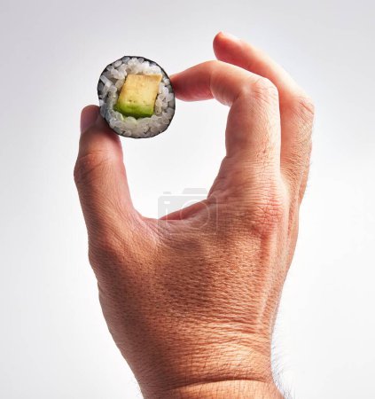 Foto de Primer plano de la mano de un hombre sosteniendo un trozo de sushi sobre un fondo blanco, haciendo hincapié en la frescura y la cocina. - Imagen libre de derechos