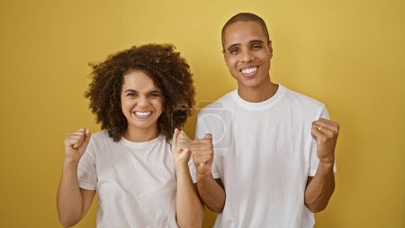 Stunning couple exuding confidence, celebrating love with bright smiles, standing together against a vibrant yellow, isolated background