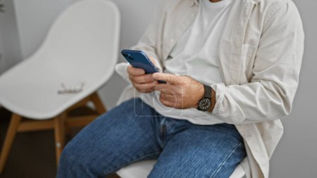 Photo for Caucasian man using smartphone sitting on chair at waiting room - Royalty Free Image