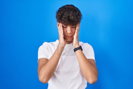 Photo for Hispanic teenager standing over blue background with hand on head, headache because stress. suffering migraine. - Royalty Free Image